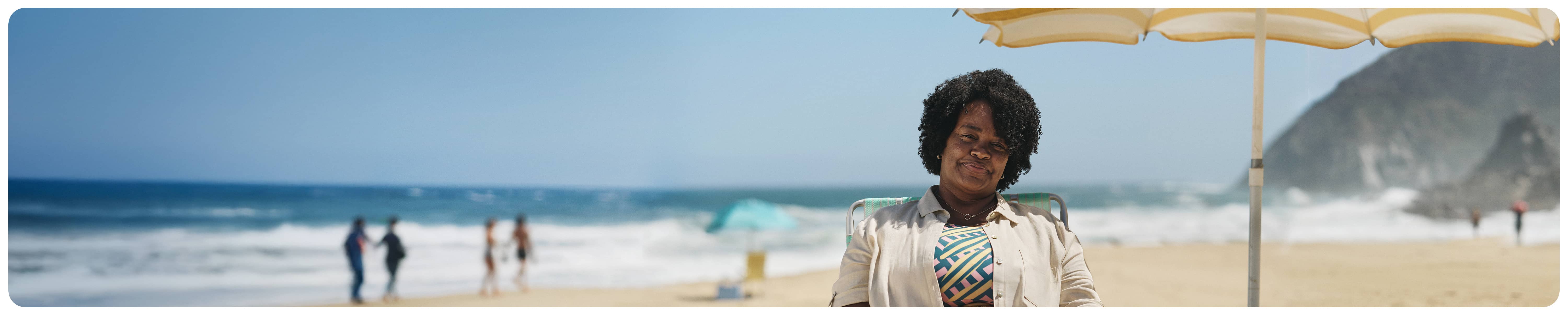 A woman sitting in a beach chair under an umbrella 